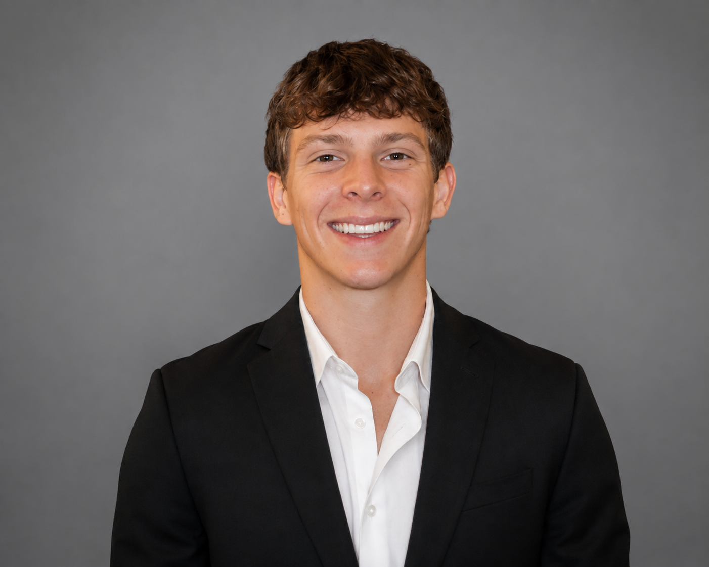 VP of Sales at TG Talent Team LLC — young man with brown hair, smiling in a black suit jacket and white shirt against a gray background.