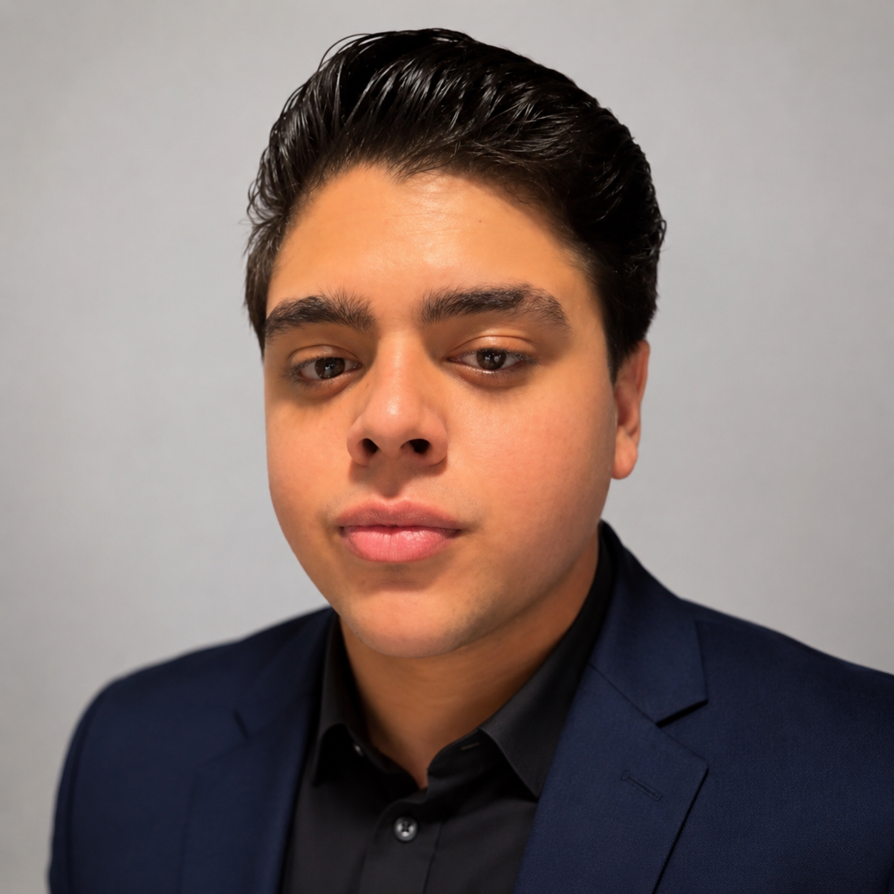 Executive-style team portrait of Giancarlo Dorta, Head of Client Acquisition, wearing a navy blazer over a black shirt, captured against a neutral gray backdrop with a polished and professional corporate aesthetic.