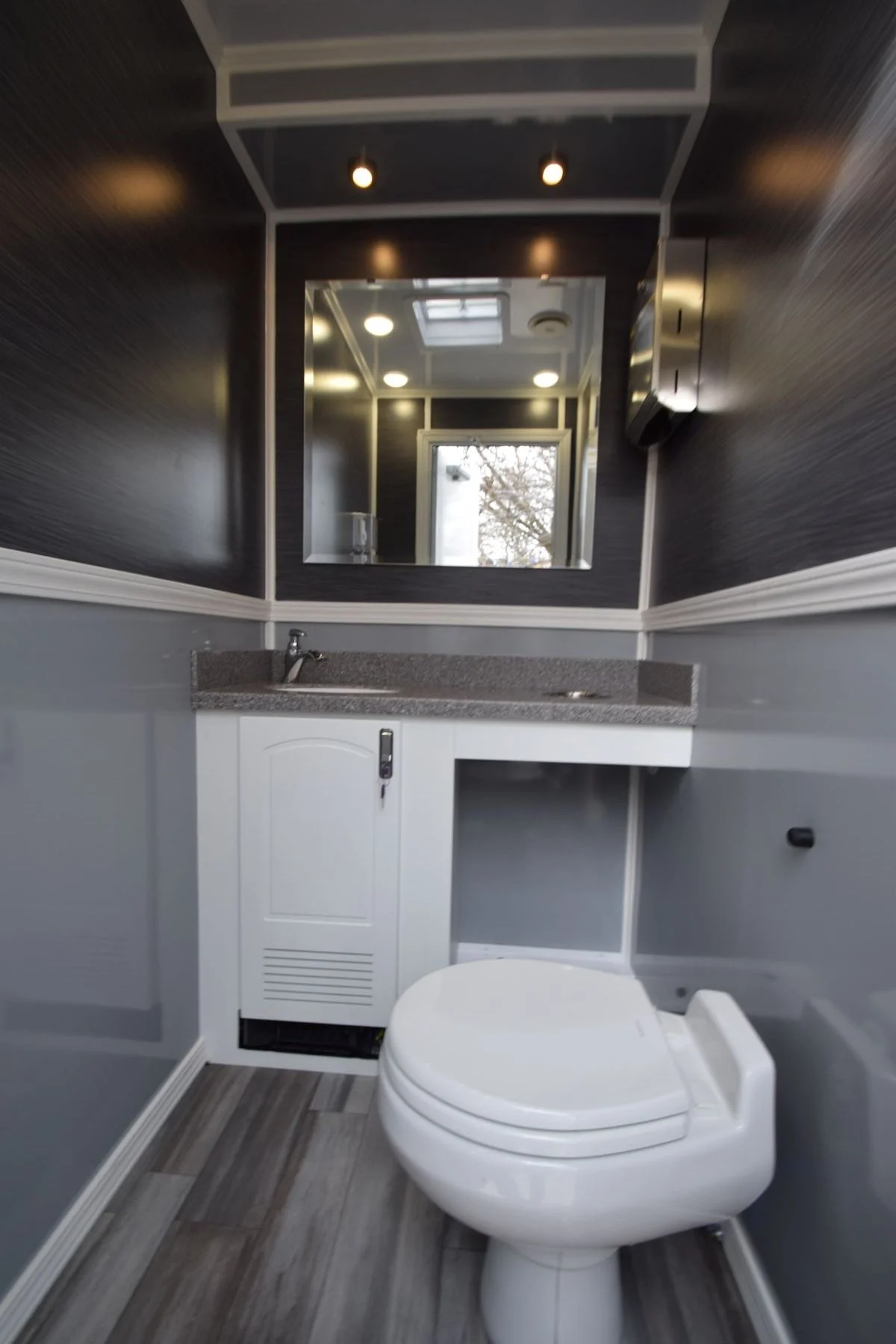 Interior view of a luxury restroom trailer showing a single private bathroom stall featuring a modern toilet, fully equipped sink with countertop space, and a wall-mounted mirror, designed with clean, upscale finishes for event use.