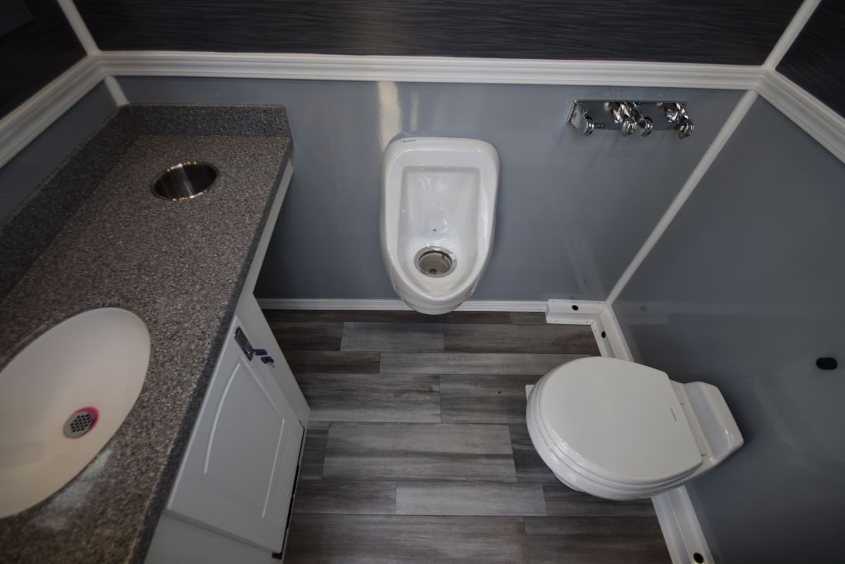A small bathroom with a grey-speckled countertop, a white porcelain sink, a urinal on the wall, a toilet, and a silver faucet fixture on a grey and blue walls with wood-look flooring.