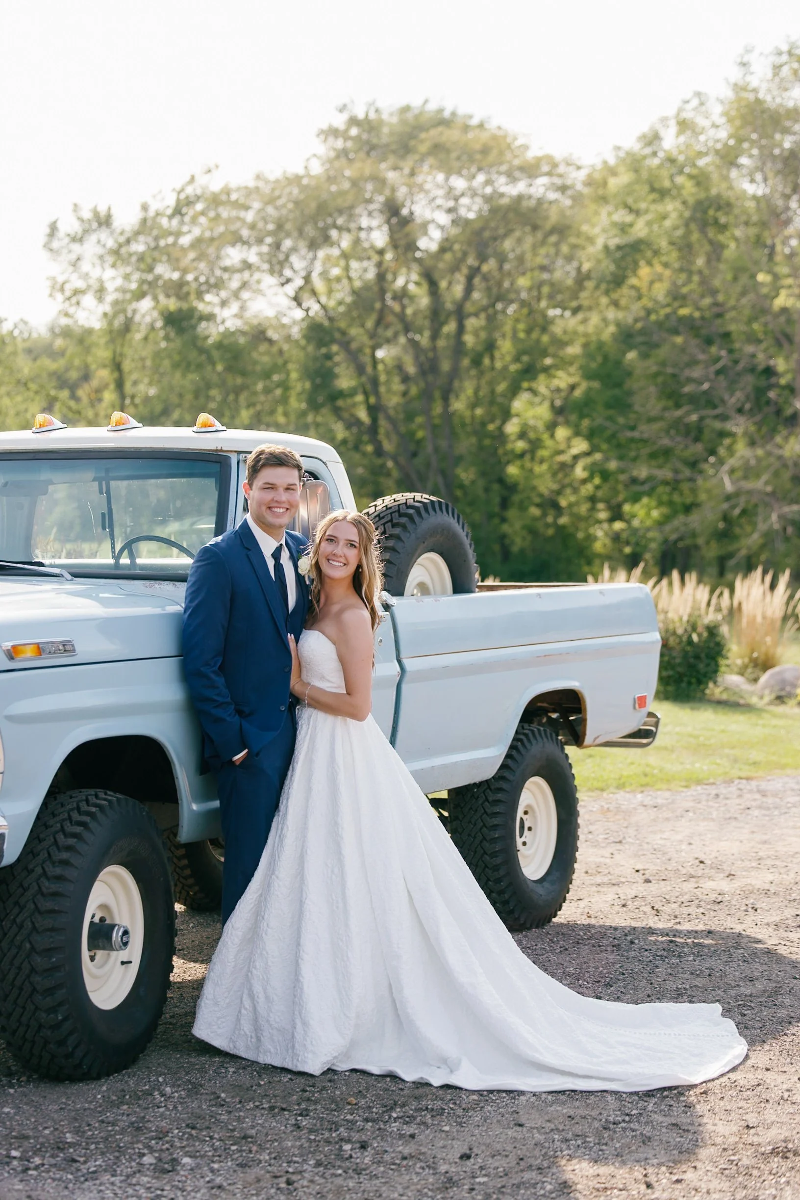 A couple standing in front of a baby blue high boy truck in their wedding attire. The Lux Loo Co Team.
