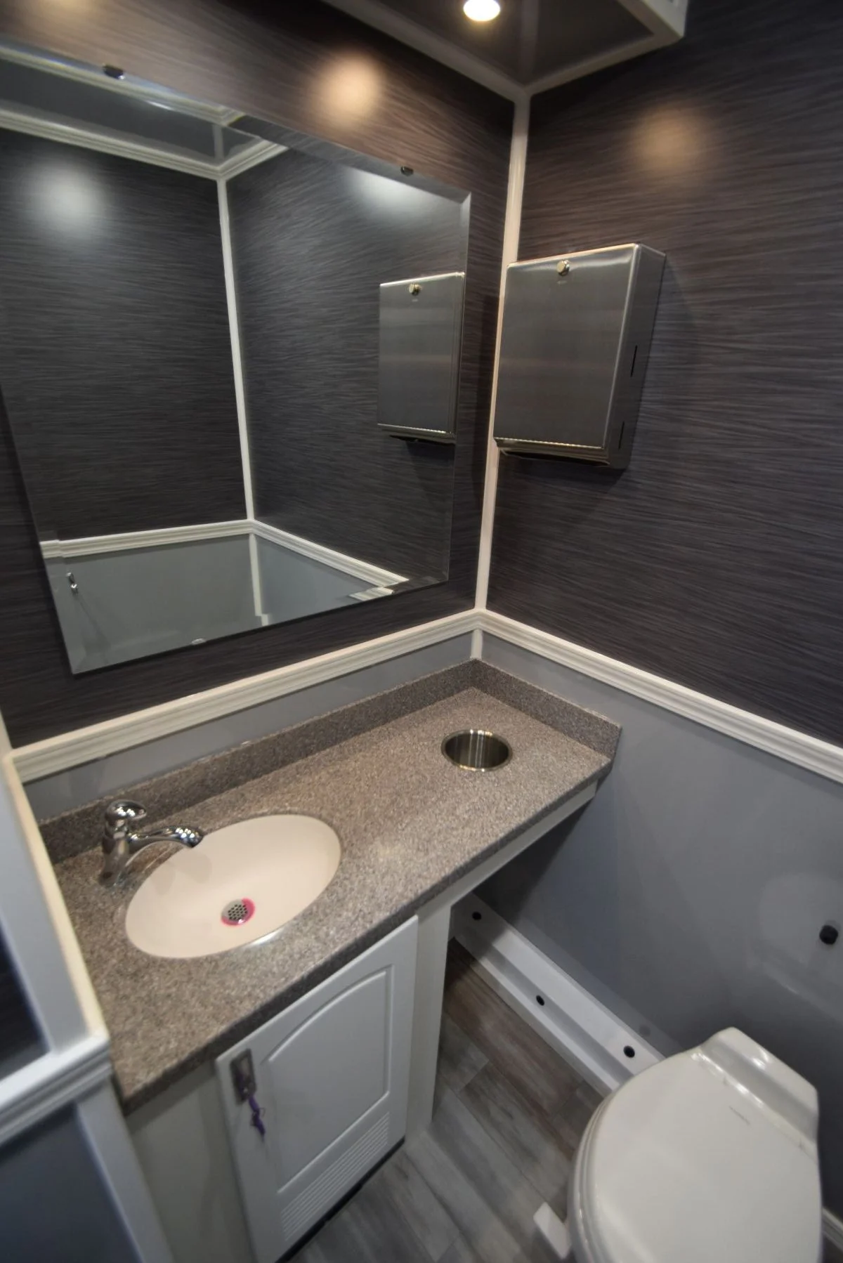 Small bathroom with a granite countertop sink, a mirror, stainless steel tissue box, and a toilet, with dark wood panel walls and a partial view of a bathtub.