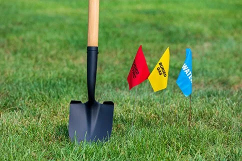 Shovel in grass beside red, yellow and blue utility marking flags