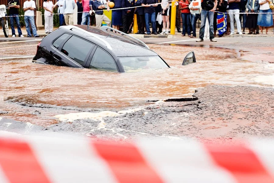 Car sunk in a roadway sinkhole behind caution tape