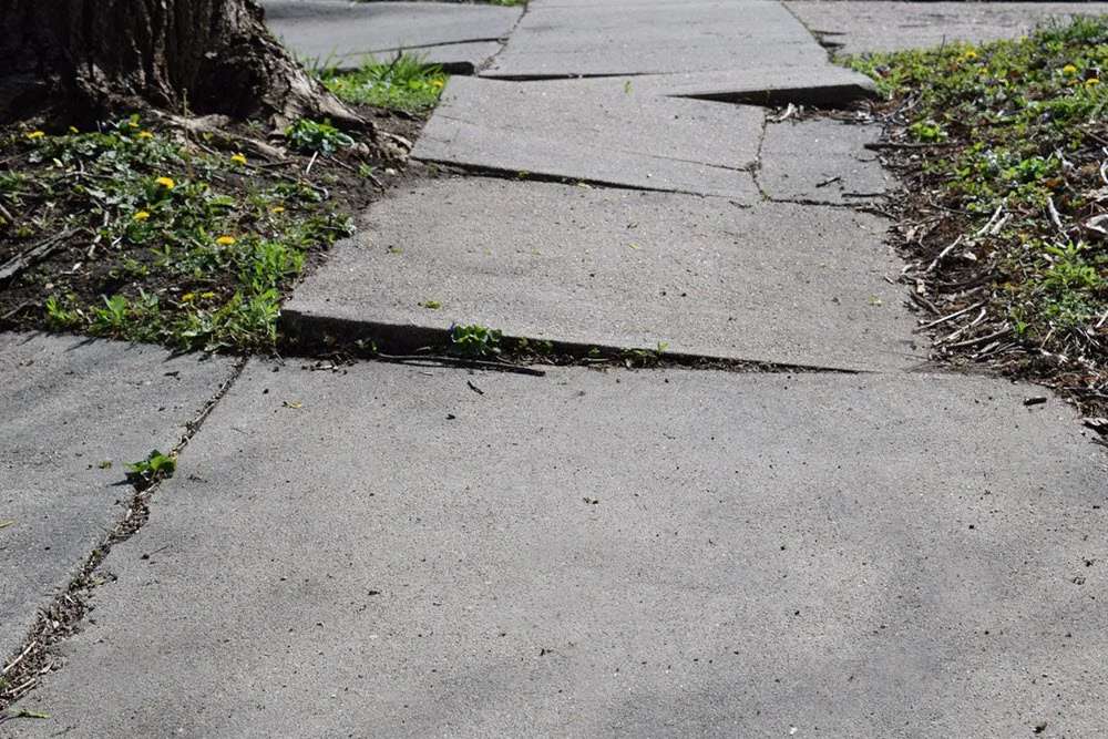 Cracked, uneven sidewalk slabs forming a trip hazard