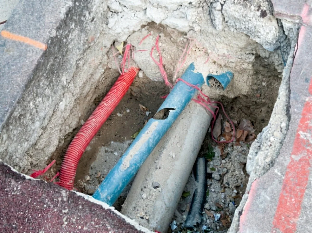 Excavation exposing buried utility lines in broken pavement