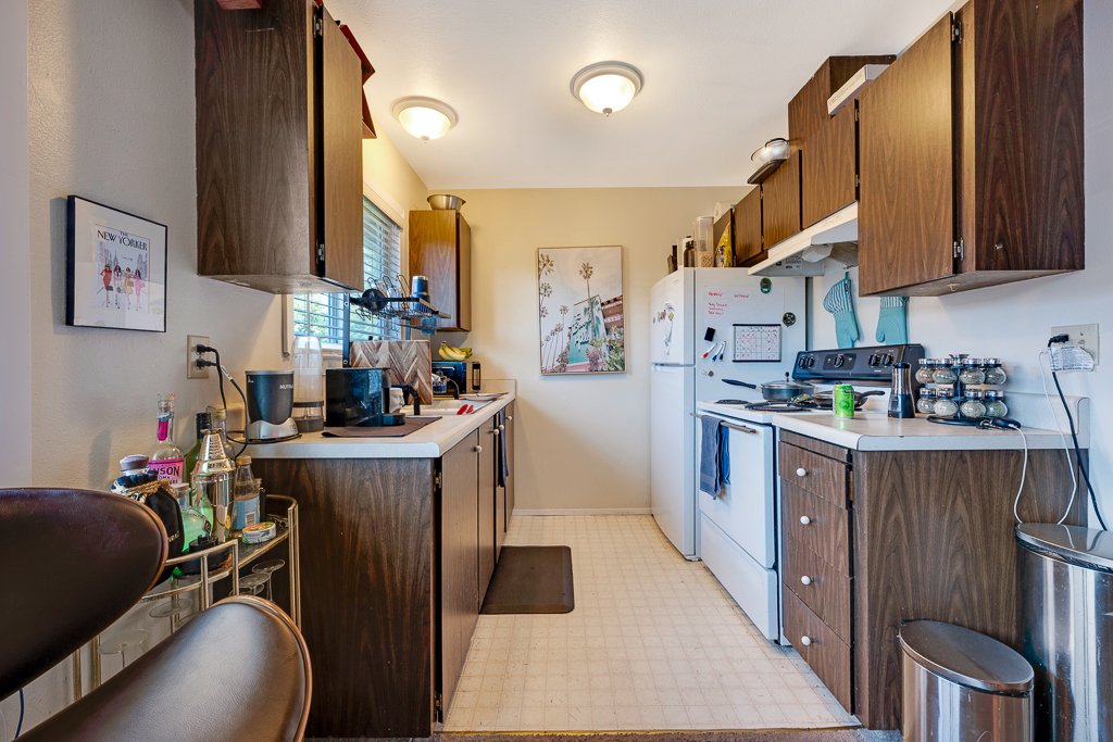 Kitchen with wooden cabinets, white appliances, coffee maker, microwave, and various kitchen items, with a small window and framed picture on the wall.