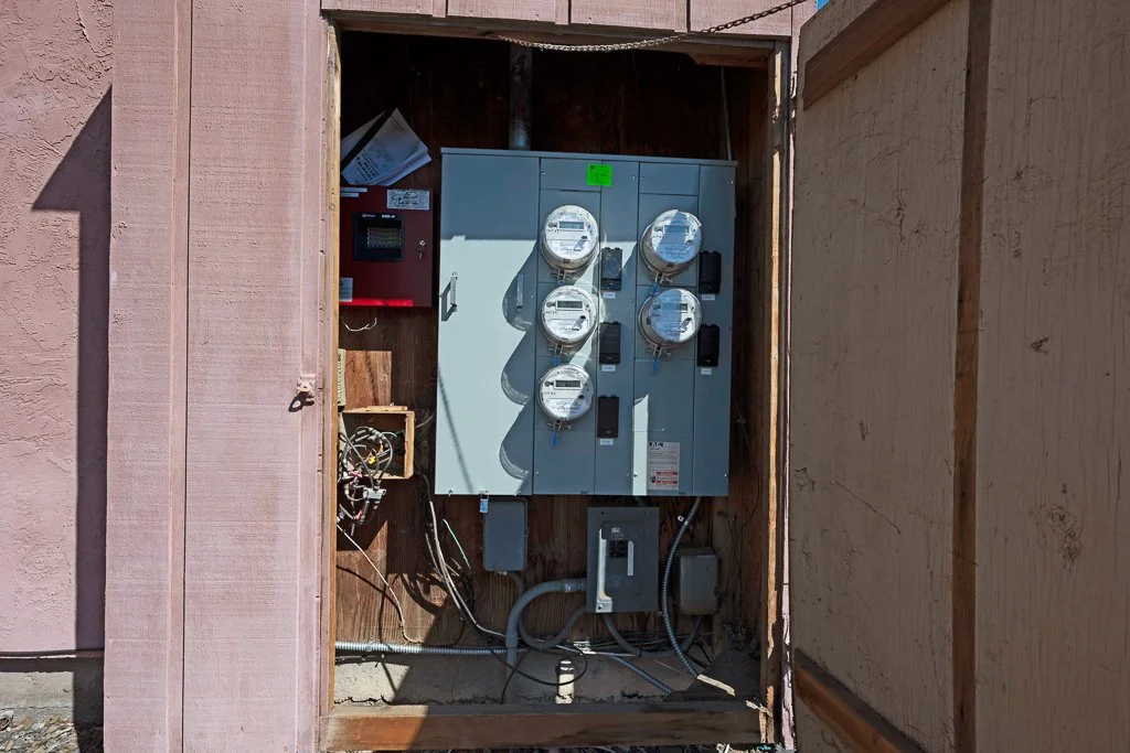 Electrical meter box with multiple meters, wires, and electrical panels inside a wooden enclosure.