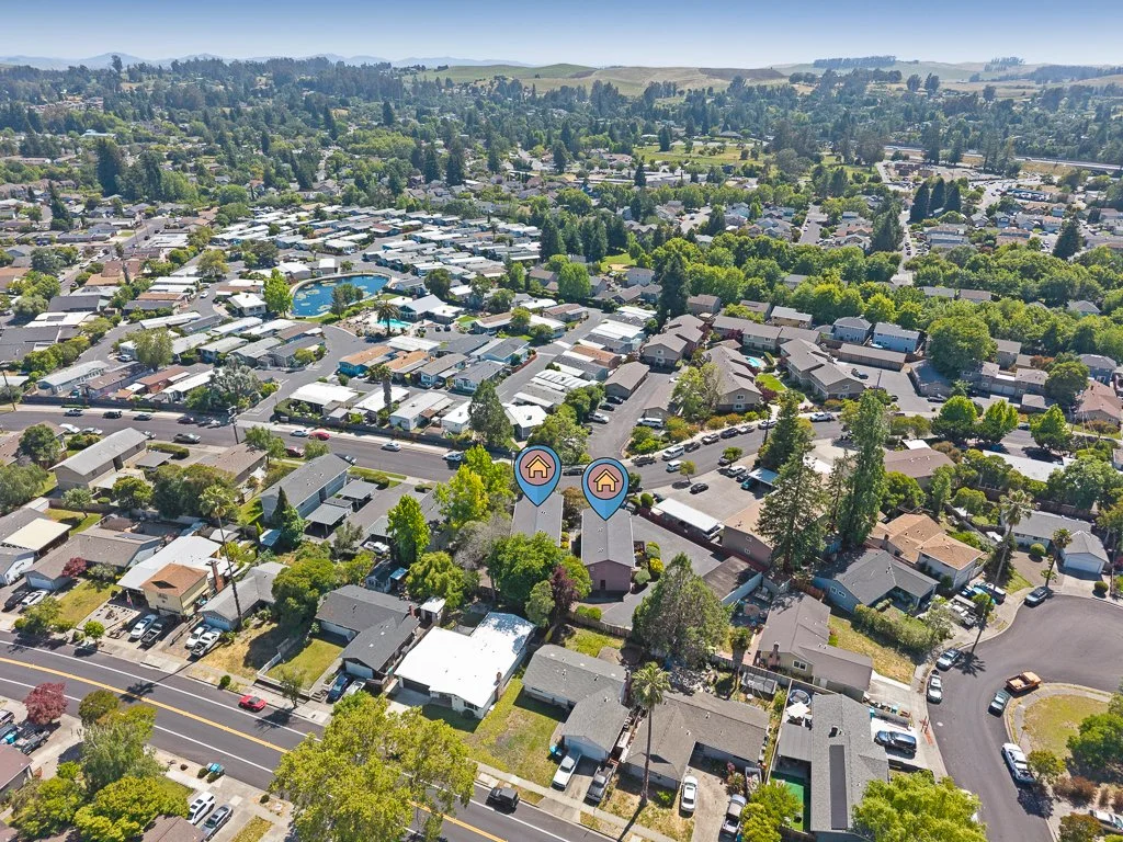 Aerial view of a suburban neighborhood with houses, trees, a community pool, and cars parked on streets.