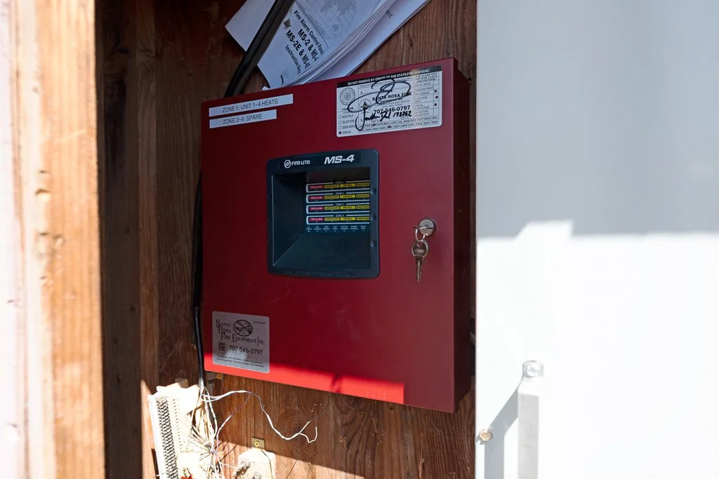 A red fire alarm control panel mounted on a wooden wall with a key in the lock and several stickers and labels on it.