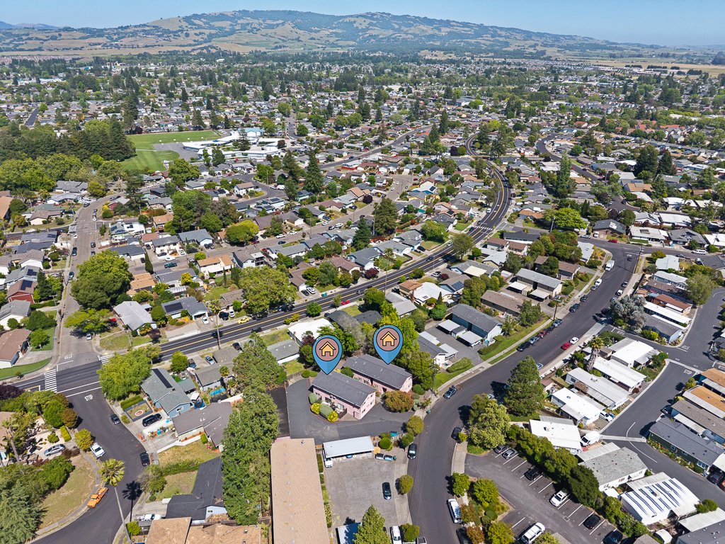 An aerial view of a suburban neighborhood showing houses, roads, and trees with hills in the background.