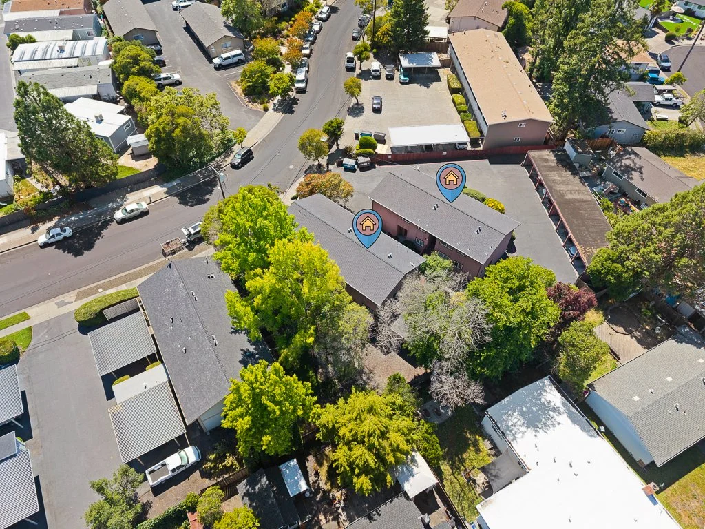 Aerial view of a residential neighborhood with several houses, trees, and parked cars, with two houses marked with house icons.