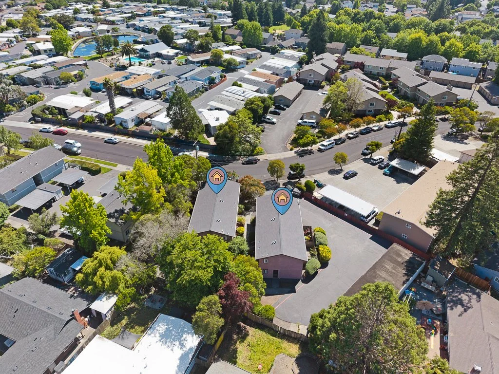 Aerial view of a suburban neighborhood with houses, trees, and parked cars, including two marked homes with house icons.