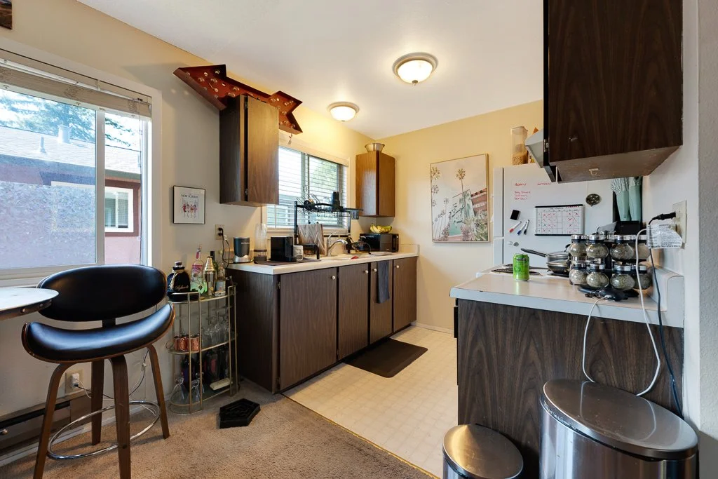 Kitchen with dark wood cabinets, white countertops, a white refrigerator, a small round table with a black and wood chair, and various kitchen appliances and utensils.