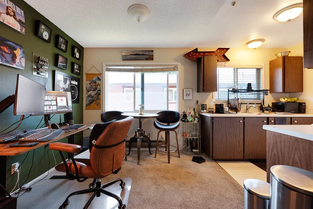 A small apartment kitchen and workspace with a desk, computer, and chairs.
