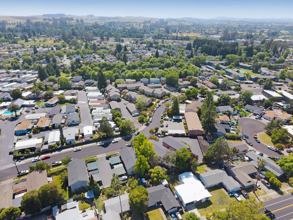 Aerial view of a suburban neighborhood with houses, trees, and streets, extending to a distant hilly horizon.
