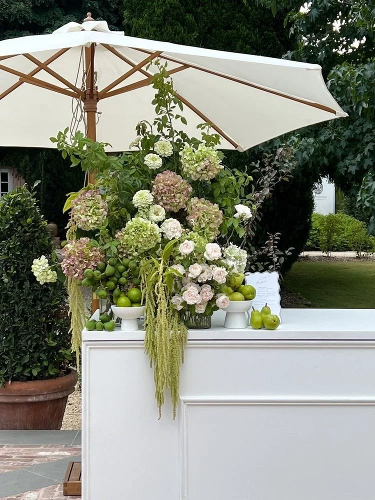 wedding reception bar with umbrella and large floral arrangements hydrangeas and greenery