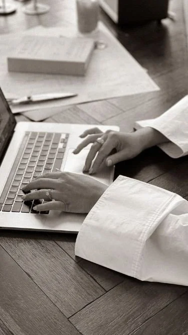 Person typing on a laptop at a desk with a notebook and pen nearby.
