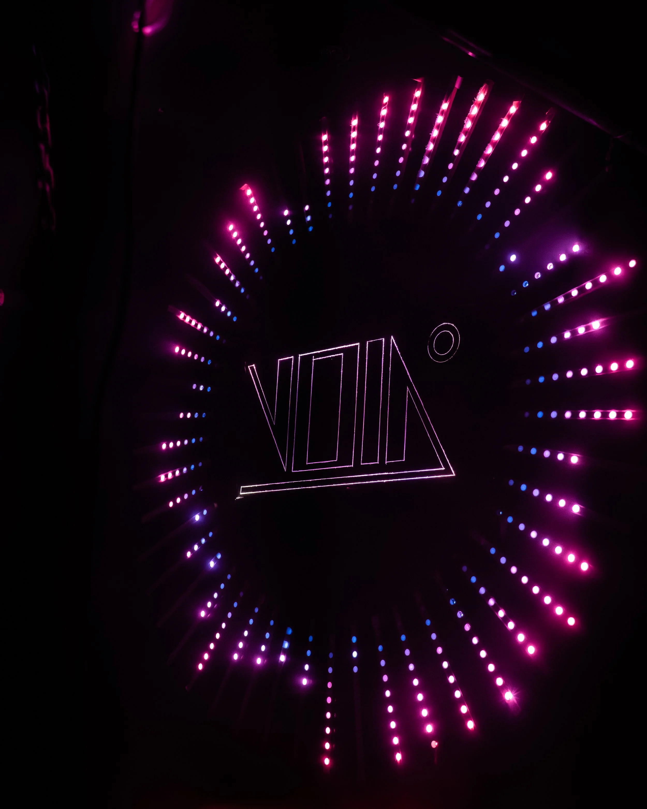 Blick auf eine Neon-Lichtinstallation mit rosa, violetten und blauen Lichtern, die einen kreisförmigen Rahmen bilden, mit dem Schriftzug 'VIXIN' im Zentrum.