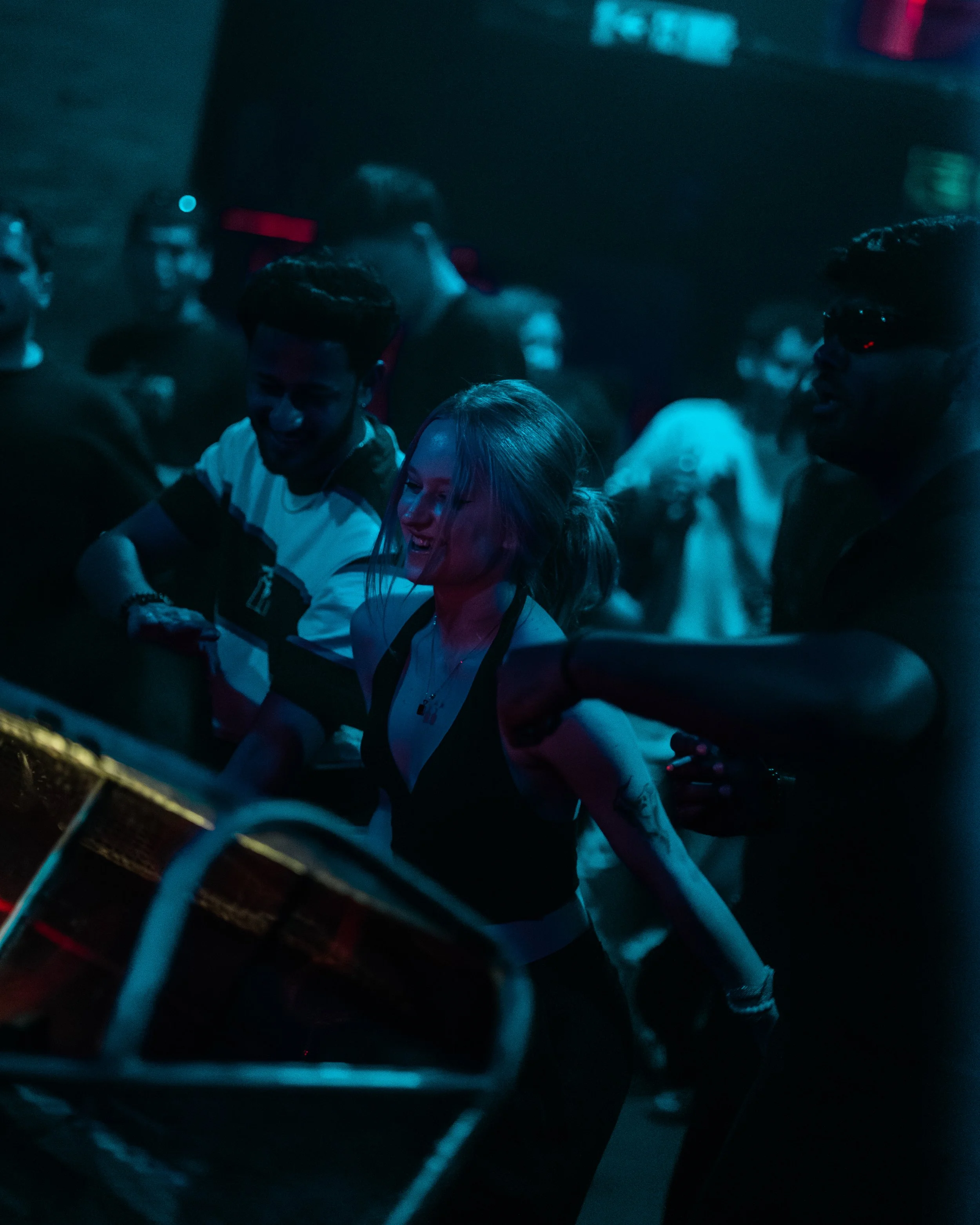 Menschen tanzen und lachen in einer dunklen, neonbeleuchteten Umgebung, vermutlich auf einer Party oder in einem Club.