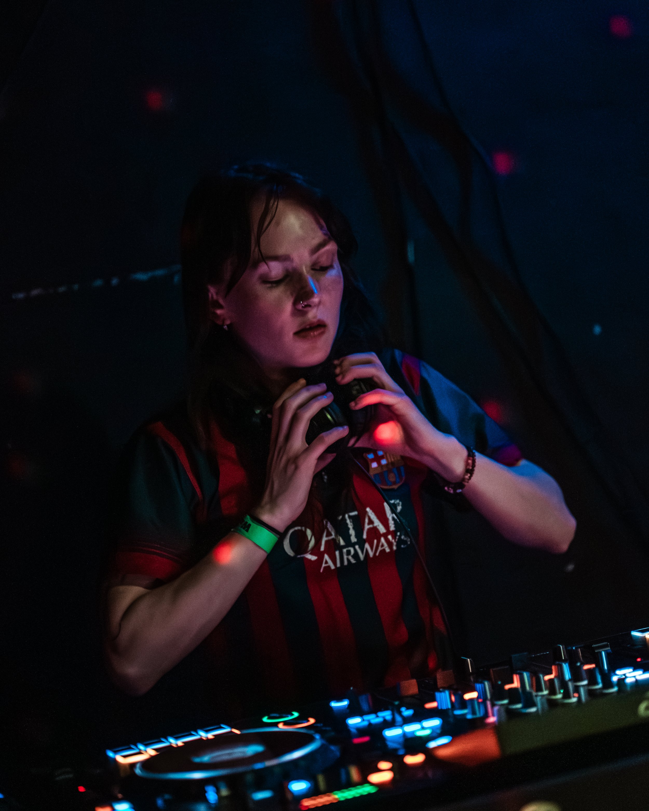Junge Person beim DJing in einem dunklen Raum mit bunter Lichtbeleuchtung, Bedienung eines DJ-Controllers.