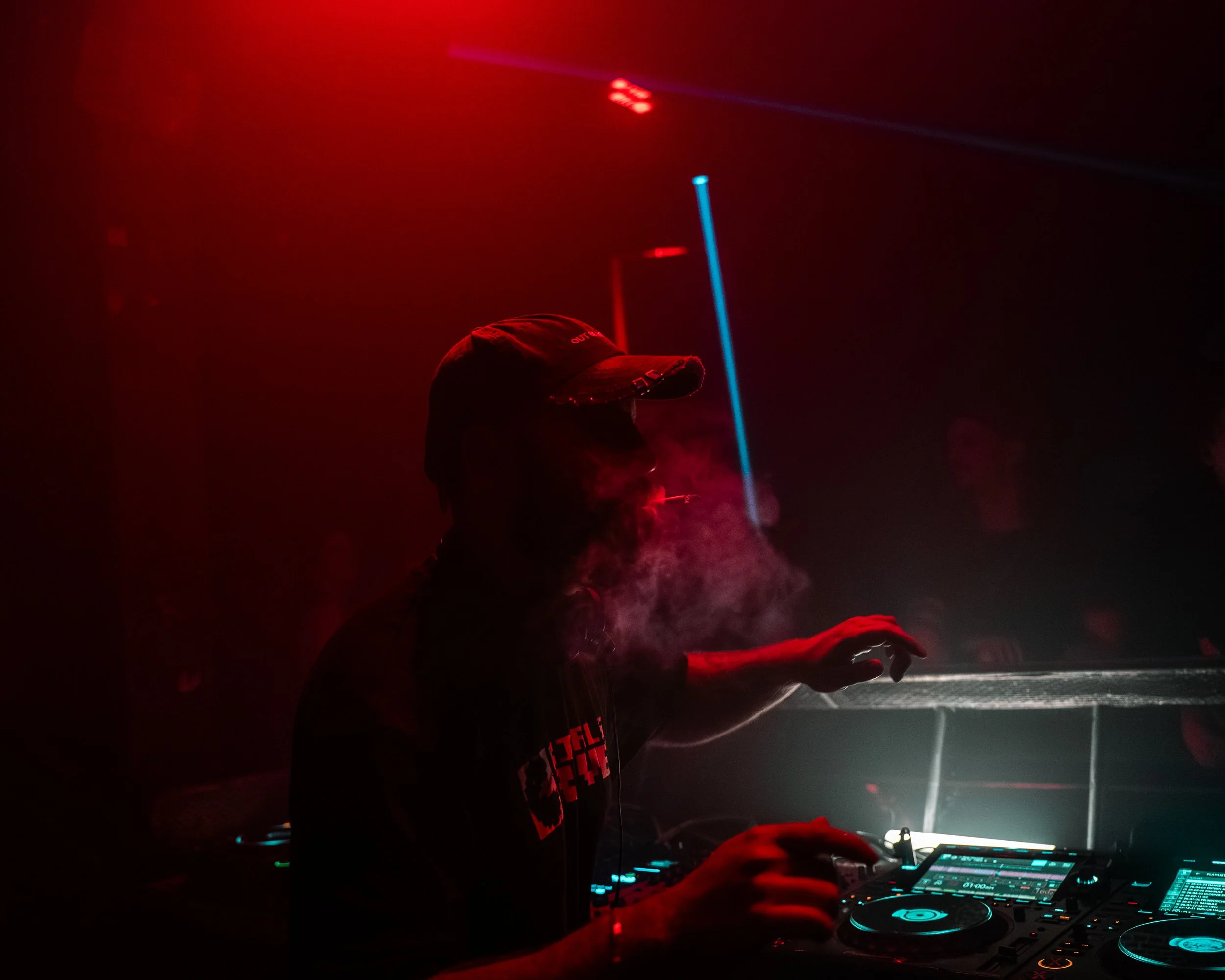 DJ mit DJ-Controller und Beleuchtung im Club, rot-und-blau Beleuchtung, Person mit Cap, Musikproduktion während einer Party.