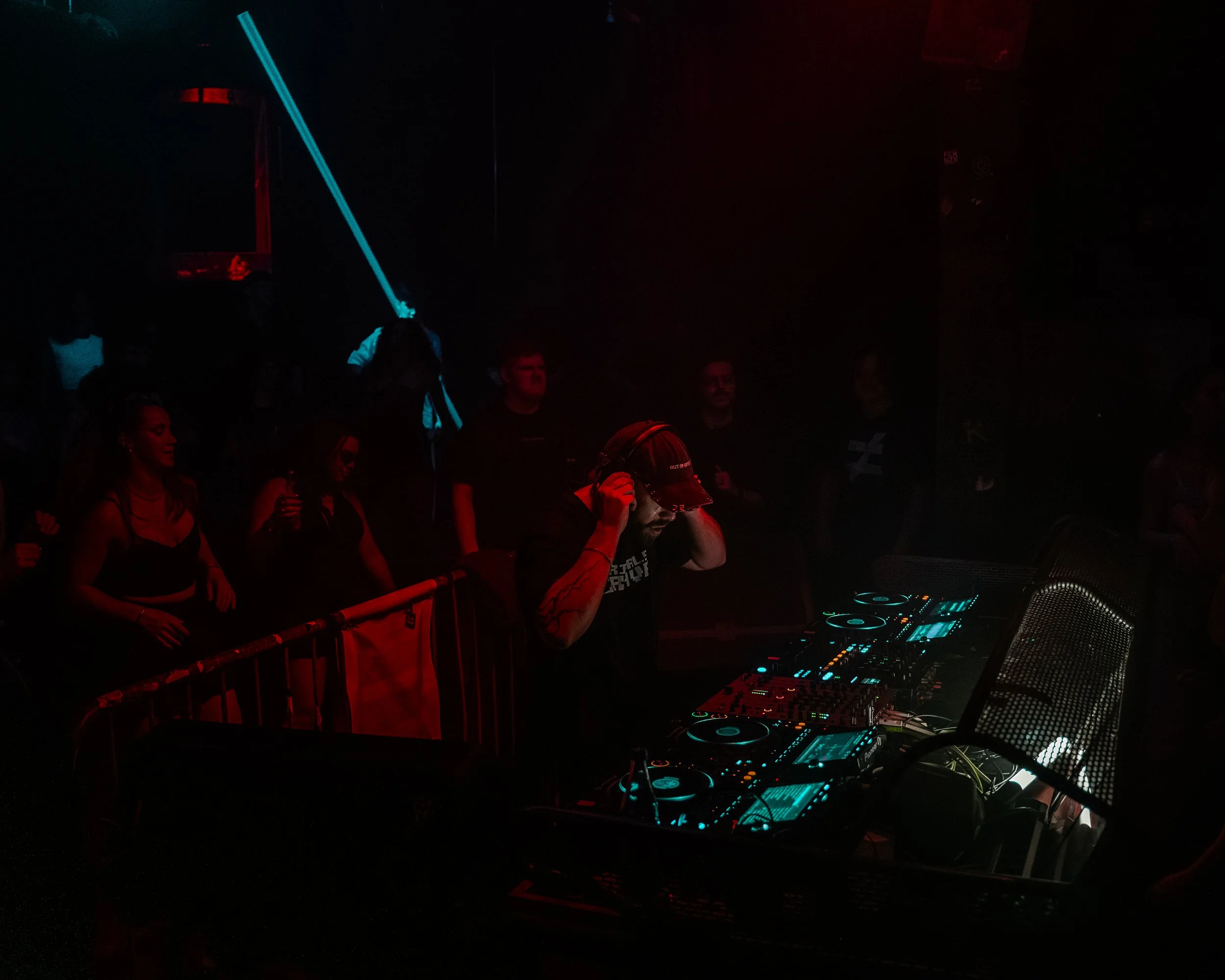 Menschen tanzen und feiern in einem dunklen Club mit DJ-Setup, leuchtenden Lichtern und dunkler Atmosphäre.