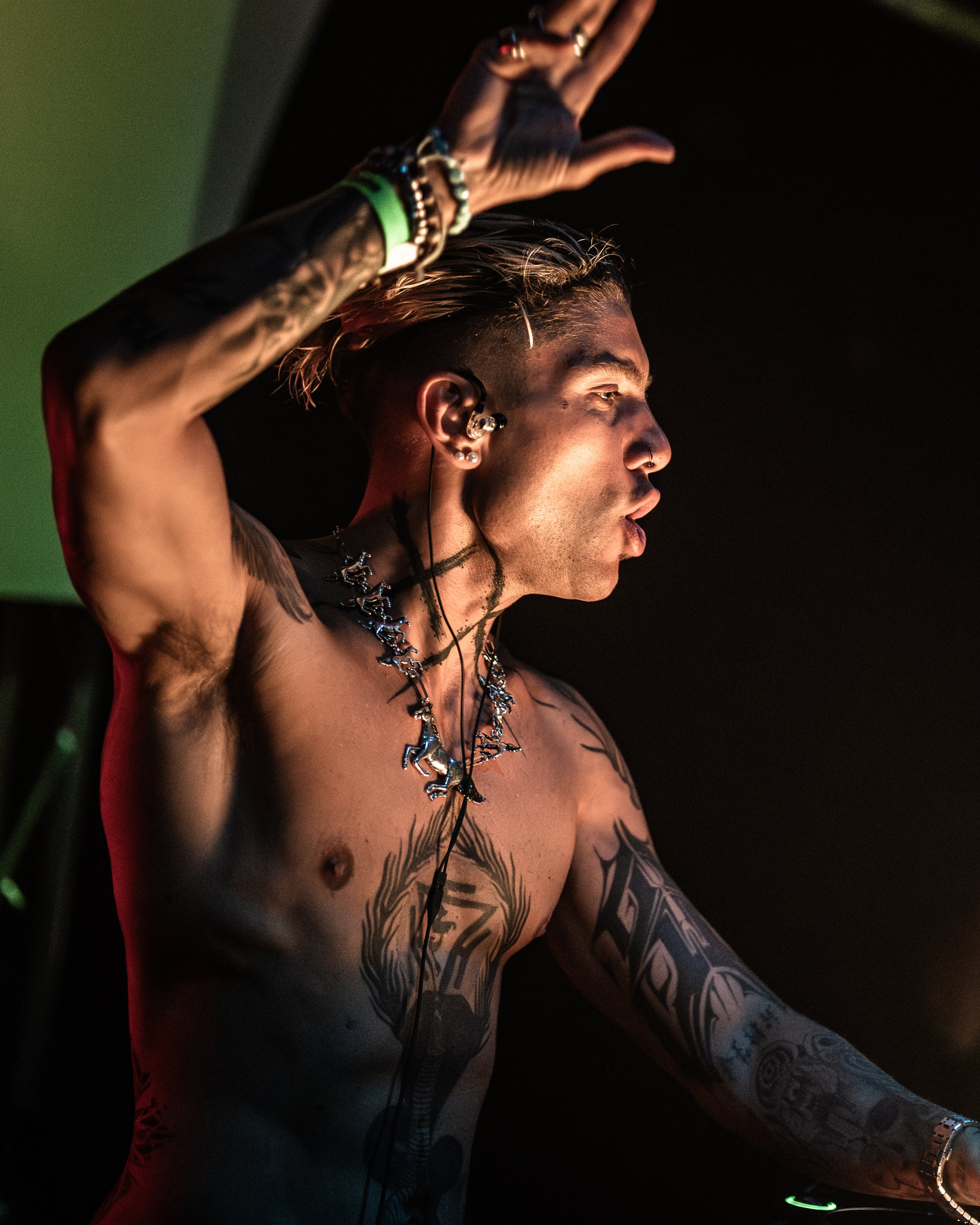 Ein Mann mit Tattoos, Piercings und mehreren Armbändern, der im Dunkeln Musik hört und an einem DJ-Controller arbeitet.
