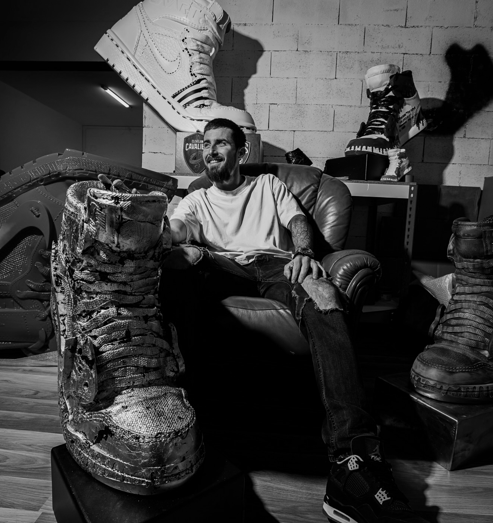 Julian Cavaillé sitting on a leather armchair in a room with sports shoes and basketball shoes displayed on shelves behind him, black and white photo.