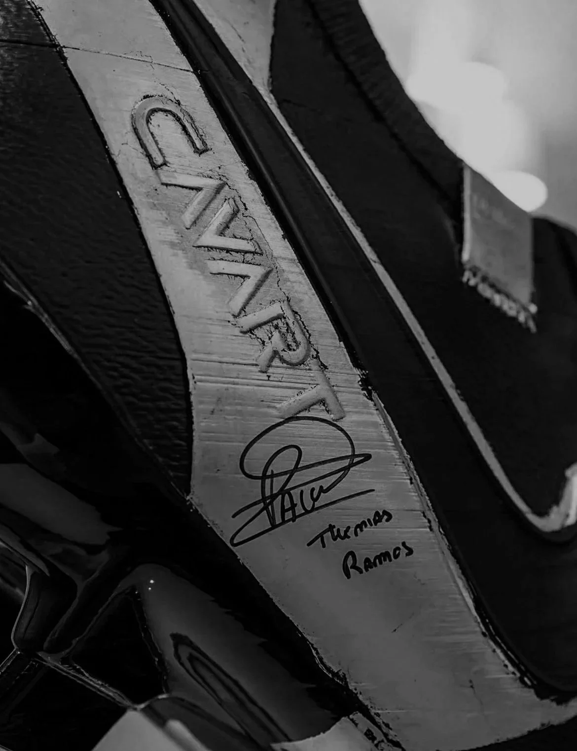 Close-up of a black and silver sneaker sculpture and name 'GWIN' engraved, along with a signature and the name 'Theresa Ramos'.