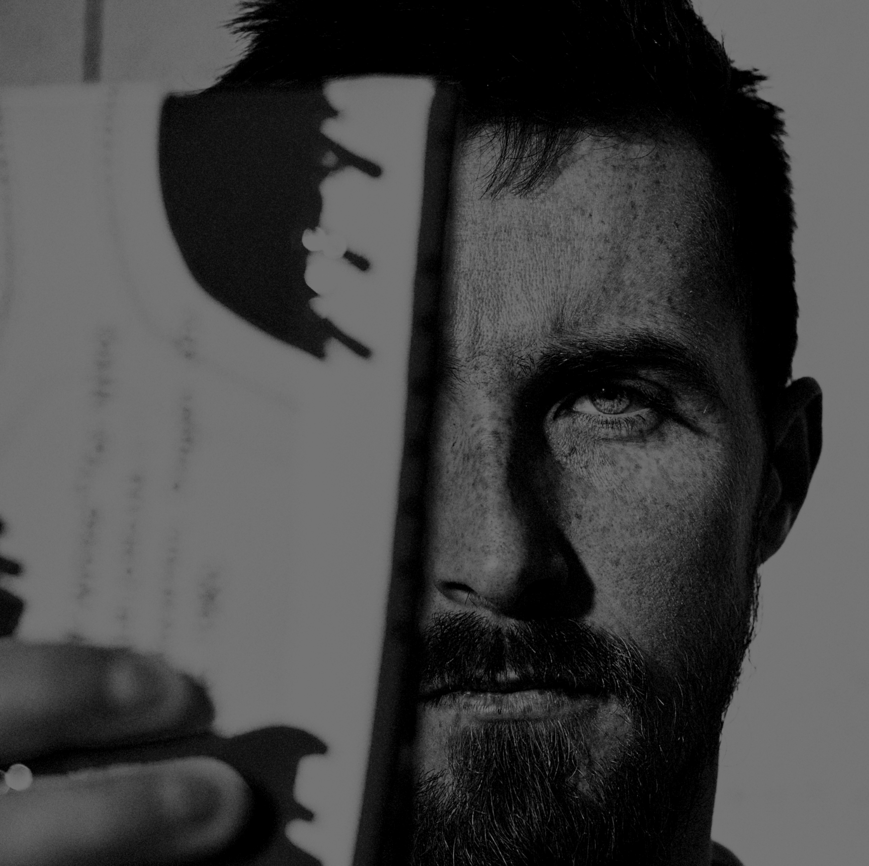 Julian Cavaillé holding a photograph of himself up to his face, partially covering it. The photo is in black and white.