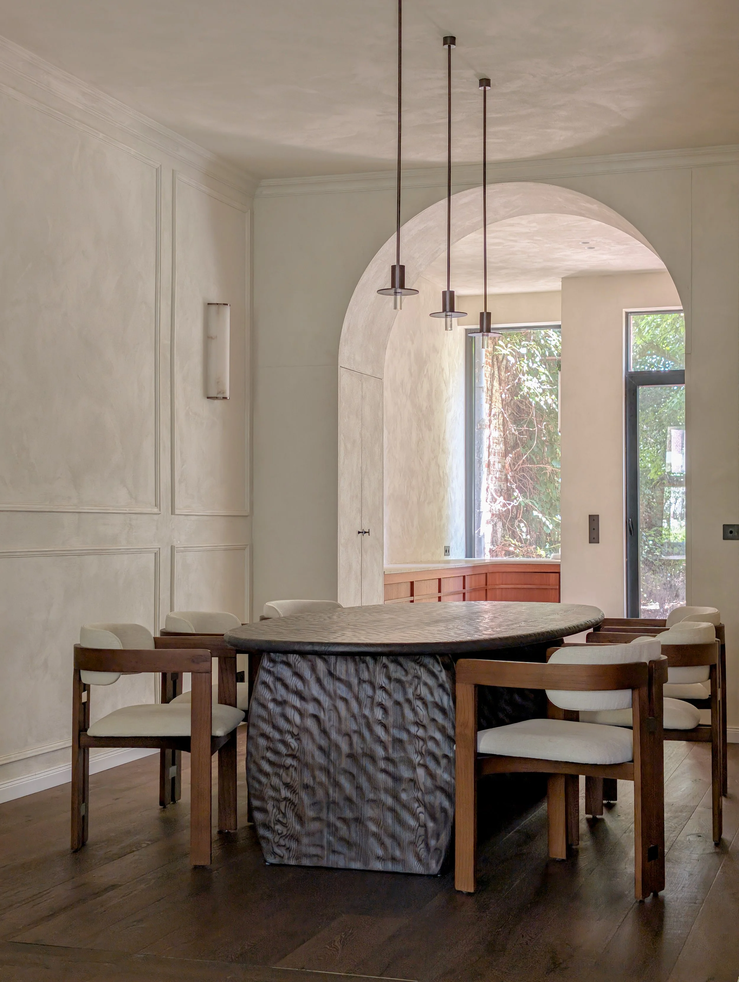 Eetkamer met een ronde tafel, acht stoelen, grote ramen, een boogmuur, en een moderne lichtinstallatie.