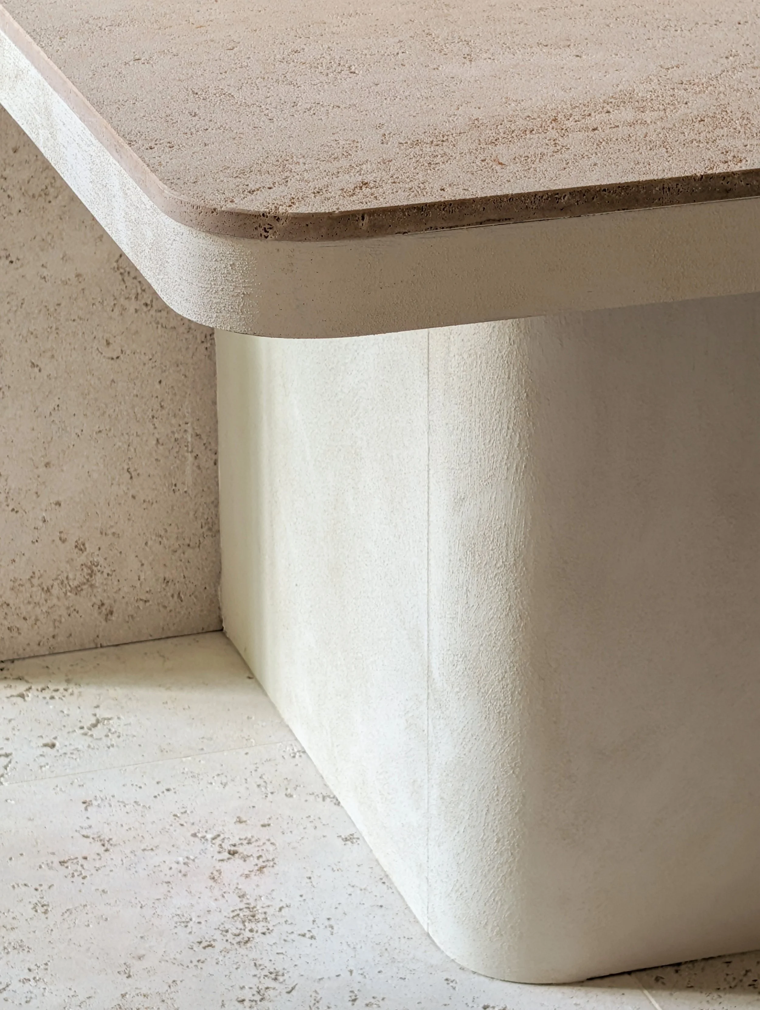 Close-up van een hoek van een beige stenen tafel en een witte muur met een muur hoek, met een vloer van vergelijkbare steenachtig materiaal.