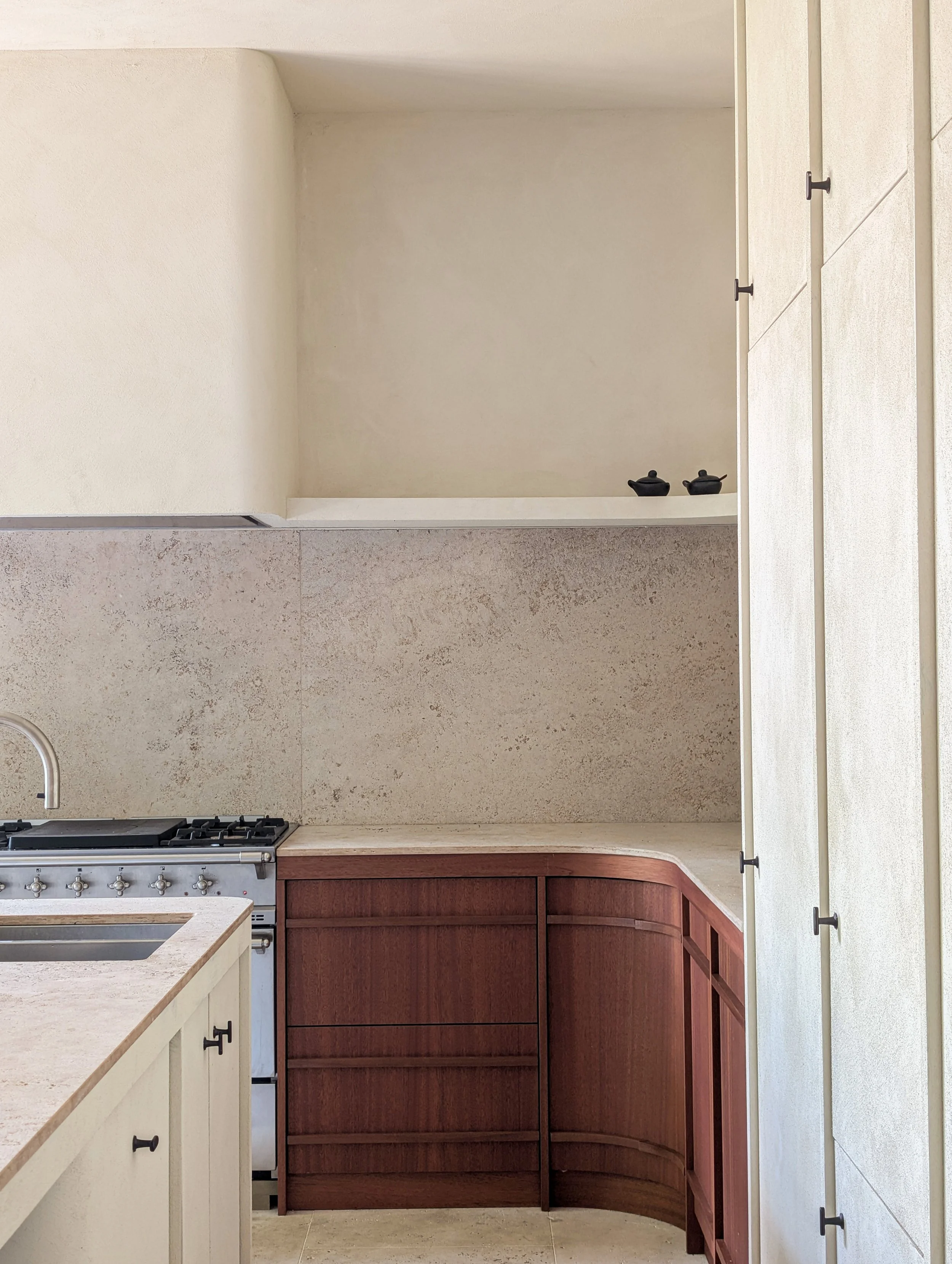 Een keuken met een lichtkleurig werkblad, een gasfornuis en kastjes van donker hout. Een lege muur op de achtergrond.