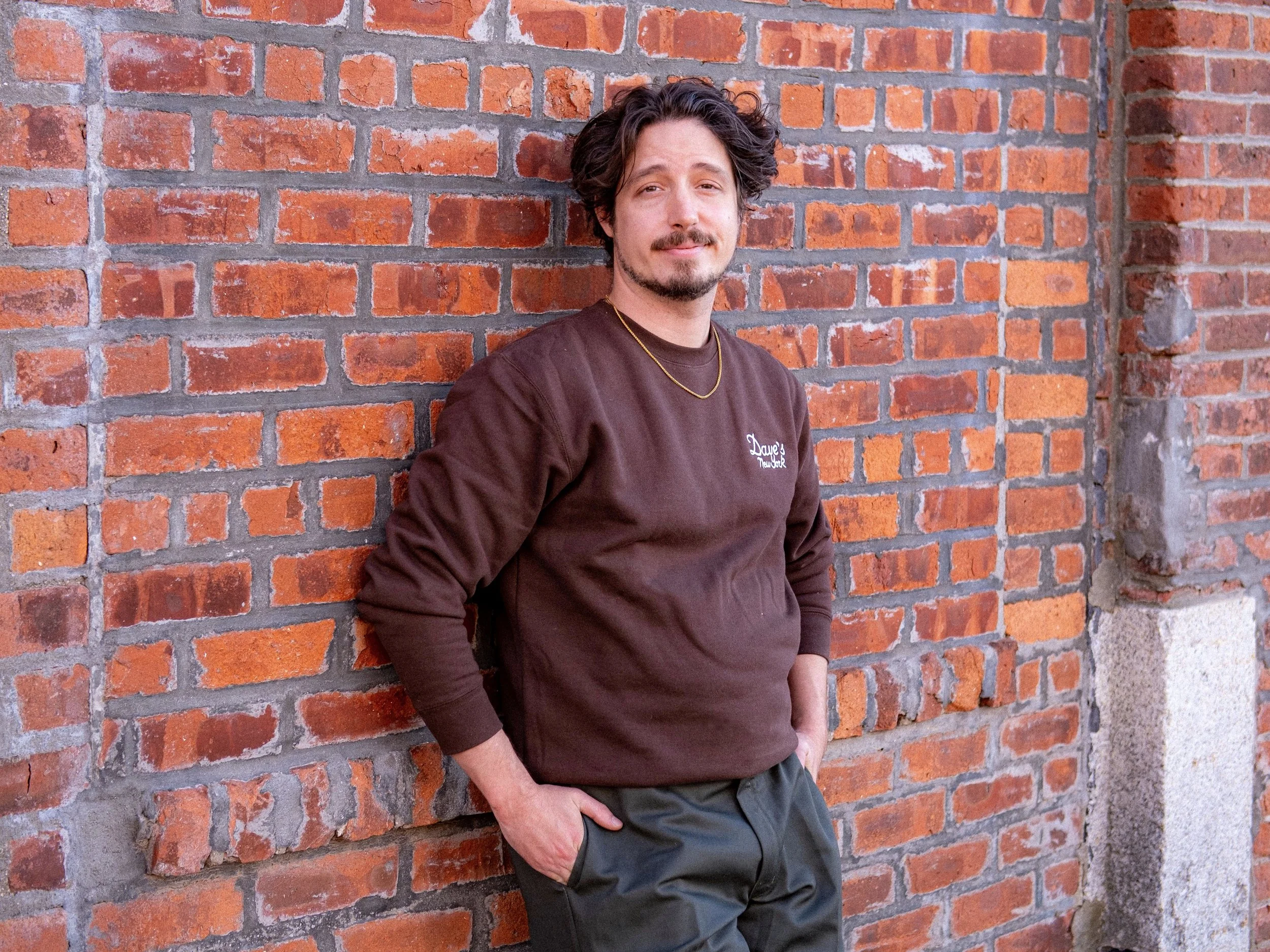 Andrew Richter: Brown hair, brown eyes. shown in a sweatshirt and green pants leaning against a brick wall