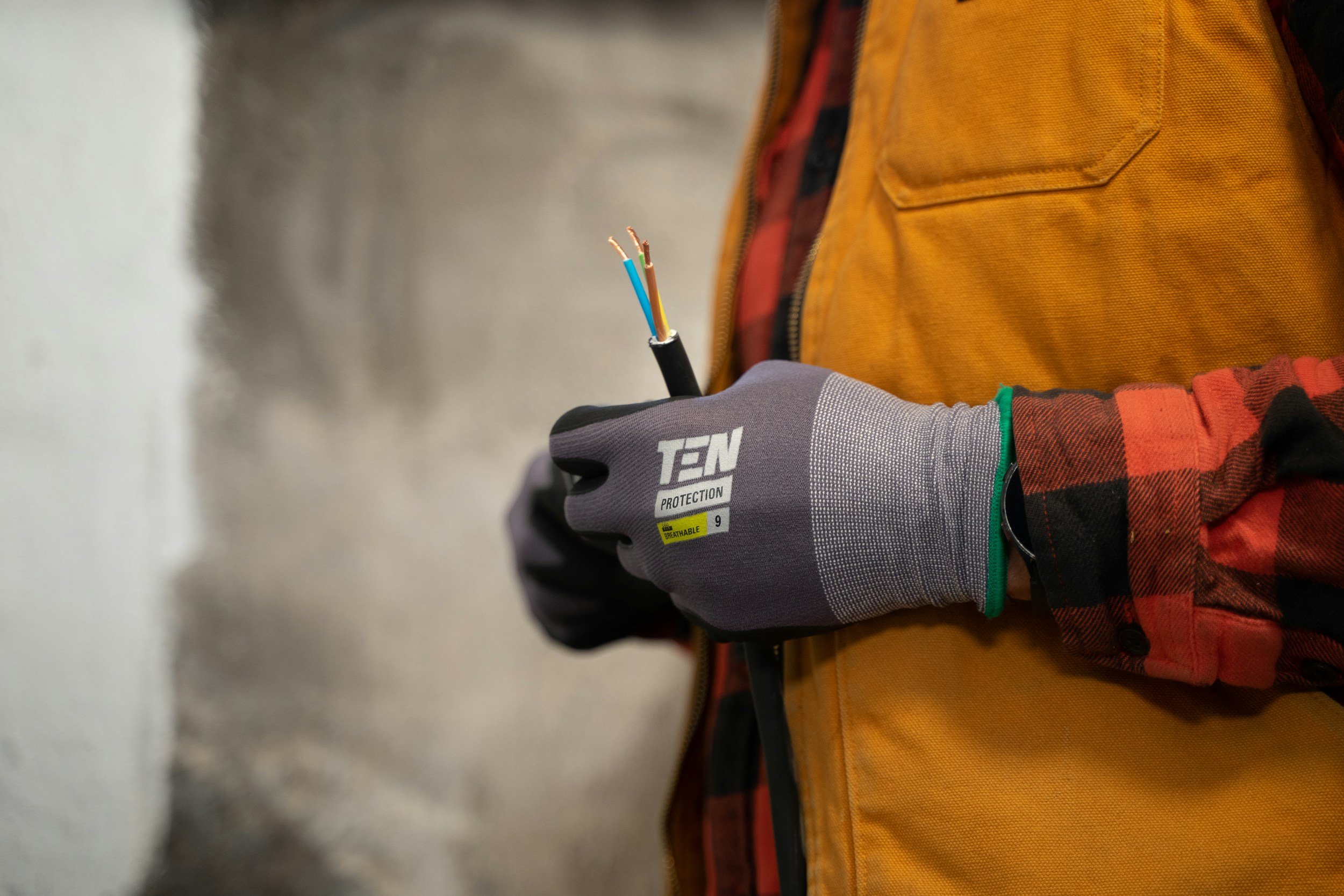 Person wearing yellow jacket and gray gloves holding a bundle of multicolored electrical wires.