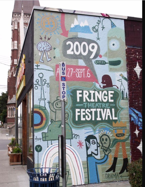 Colorful mural on a building advertising the 2009 Fringe Theatre Festival, with illustrations of a person, rainbow, and various abstract symbols, featuring text about the festival dates from September 27 to October 6.