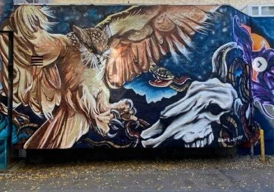 Colorful mural of a winged lion, a serpent, and a winged horse against a mountain and night sky background.