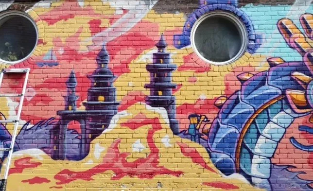 Colorful graffiti mural on brick wall featuring castles, flames, and a stylized dragon or serpent.
