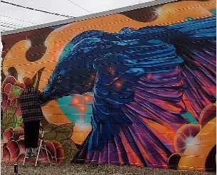 Person painting a colorful mural on a wall featuring abstract designs and vibrant colors.