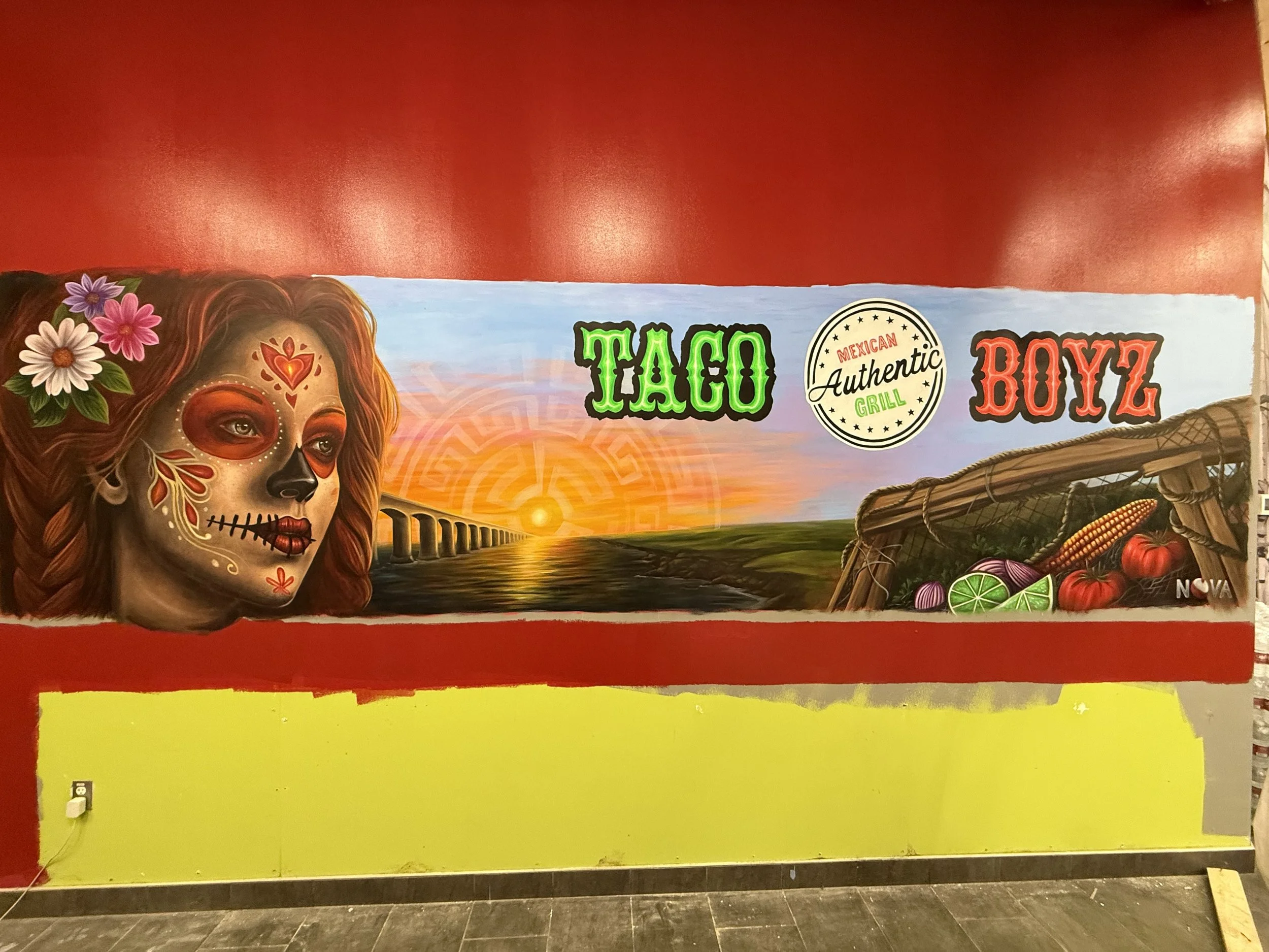 Colorful mural featuring a woman with a Day of the Dead face paint, flowers, and a sunset over a bridge, with the words 'Taco', 'Authentic', and 'Boyz' and a circular stamp that says 'Mexican Grill'.