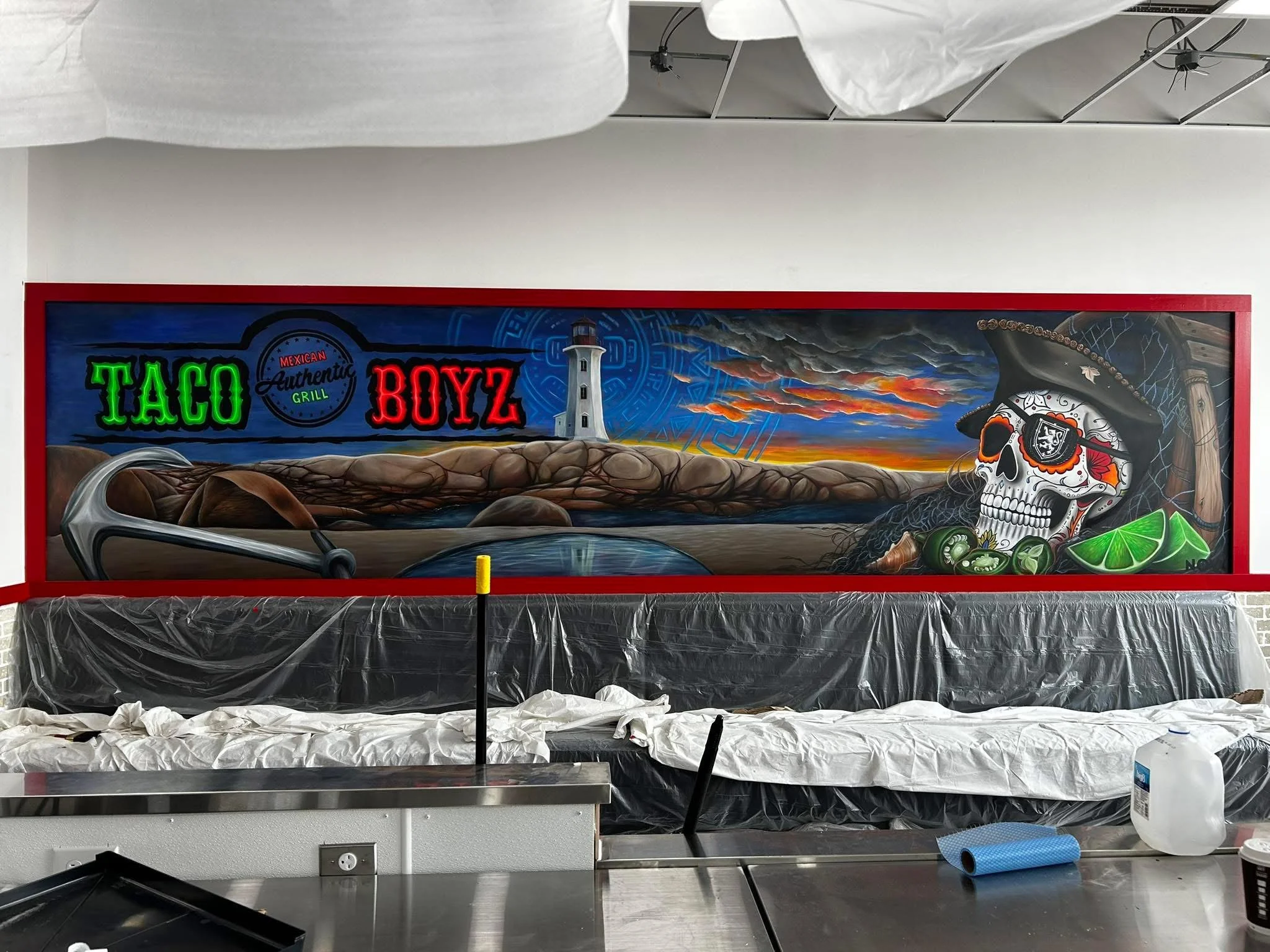 Interior of a food stand or kitchen with a colorful mural, a partial sign reading "TACO," and other items covered with protective plastic.