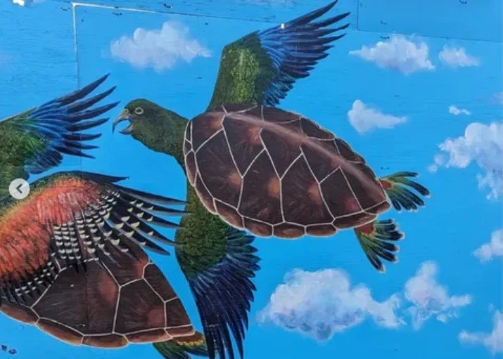 Colorful mural of flying turtles with bird wings against a blue sky background.