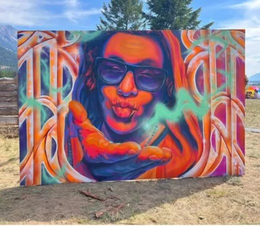 Colorful street art mural of a person with glasses blowing smoke, with vibrant swirling patterns in the background.
