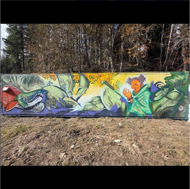 Colorful mural featuring a green alligator with a red tongue and sharp teeth, alongside a woman with curly hair playing a flute, surrounded by lush green foliage and yellow flowers.