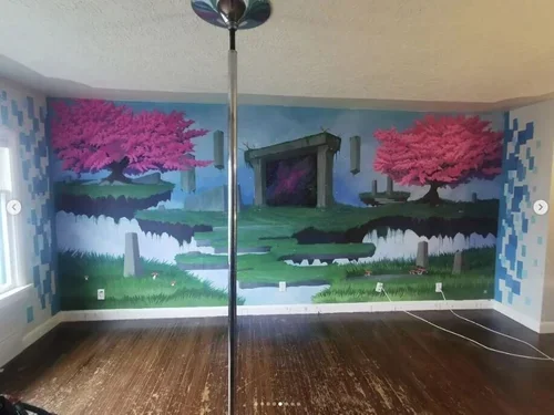 Room with a mural of a landscape featuring pink trees, a stream, and a fireplace-inspired structure on the wall.