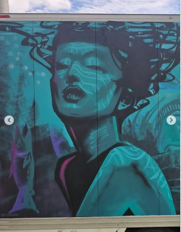 Street mural of a woman with her eyes closed, head tilted back, with flowing hair and abstract patterns in shades of blue and purple.