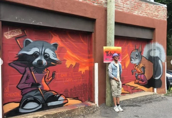Street art mural featuring cartoon raccoon and squirrel characters, with a person standing in front of the artwork. Art, street art, painter, mural, graffiti, spray paint, oil paint, montreal, commission, Futurism, retro Futurism, cyber punk, punk, b