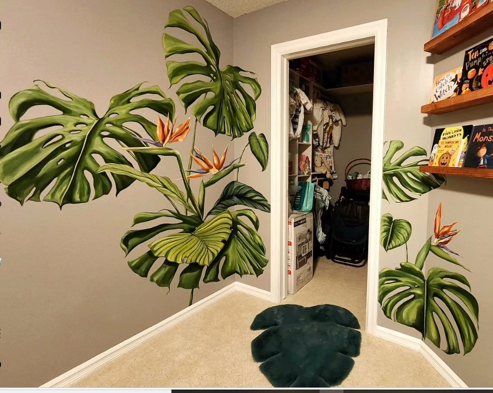 Decorative wall mural of large green monstera leaves with orange flowers in a room leading into a closet with clothing and household items.
