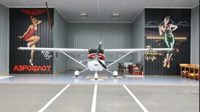 Small airplane parked inside a hangar with vintage pin-up style murals on the walls.